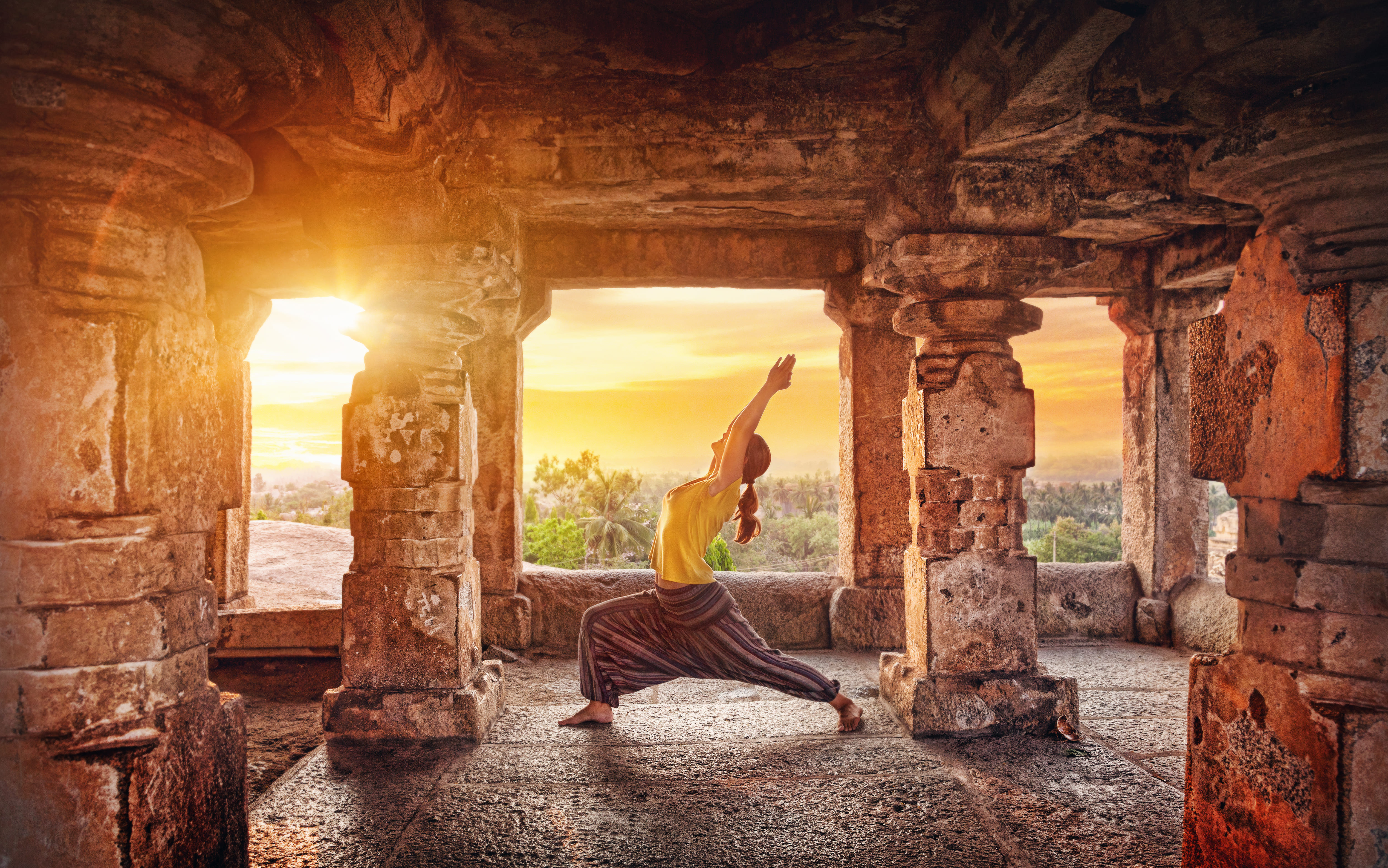 Frau entspannt sich beim Yoga. Im Hintergrund sieht man einen Sonnenuntergang. Reisearten, wie Entspannen, werden hier dargestellt