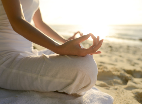 Frau sitzt am Strand und macht Yoga, welches ein immaterielles kurturelles Erbe ist