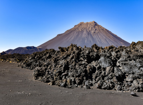Aktiver Vulkan im Hintergrund mit der erstarrten Lava im Vordergrund